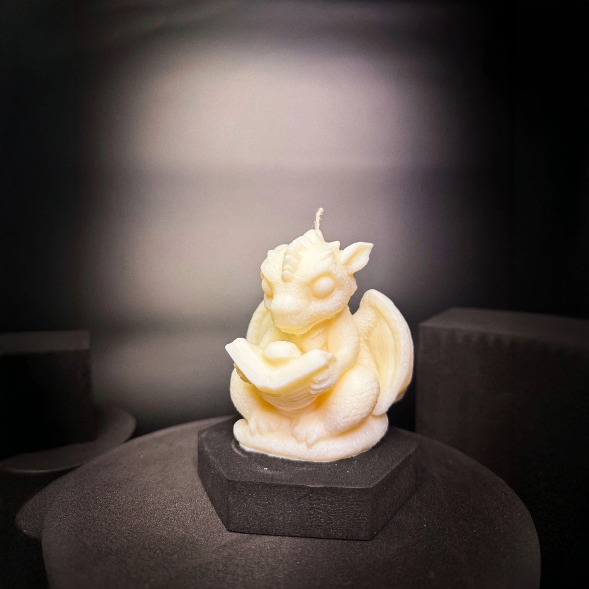 Detailed dragon shaped candle holding an open book, magical home decor piece for fantasy lovers.