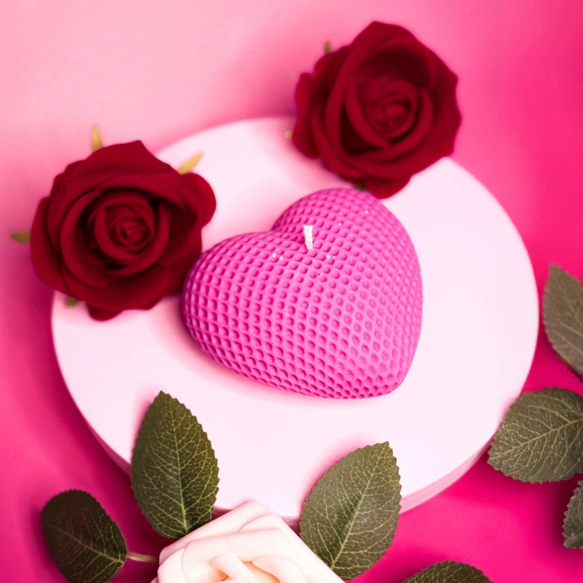 Handmade heart candle in pink soy wax photographed with red and white roses.