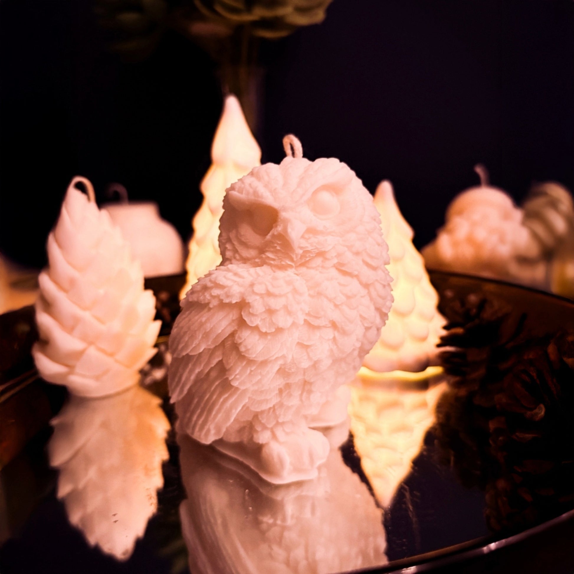 White snowy owl candle handmade in 100% soy wax, detailed winter decor candle photographed on reflective surface with warm background lights.